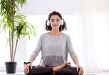 Moderne Frau mit Kopfhörern sitzt in Yoga-Botus-Haltung und meditiert | © iStock | monstArrr_