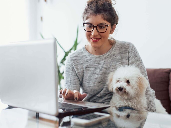 Junge Frau sitzt mit Hund vor dem Laptop | © iStock | Likoper