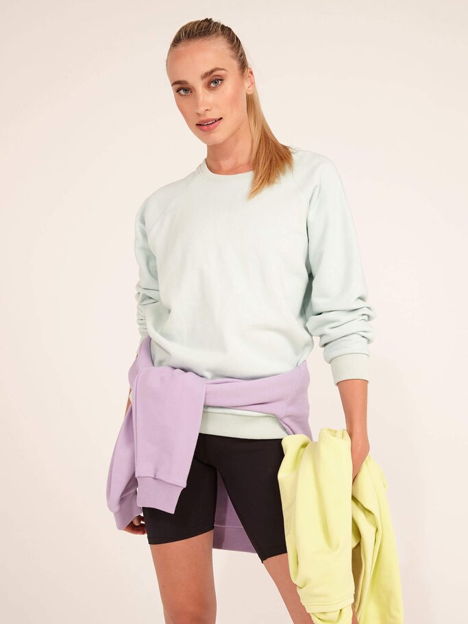 Frau im sportlichen Outfit mit drei Sweatern in Lila, Gelb und Blau von Hey Honey. | © PR