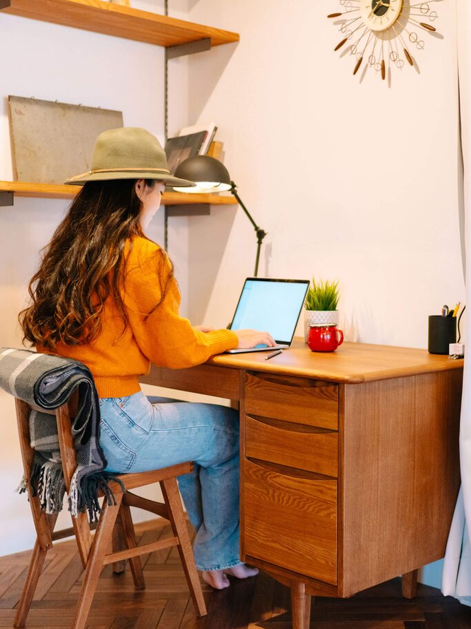 Junge Frau sitzt mit gutem Outfit und Hut am Schreibtisch im Homeoffice. | © iStock | recep-bg