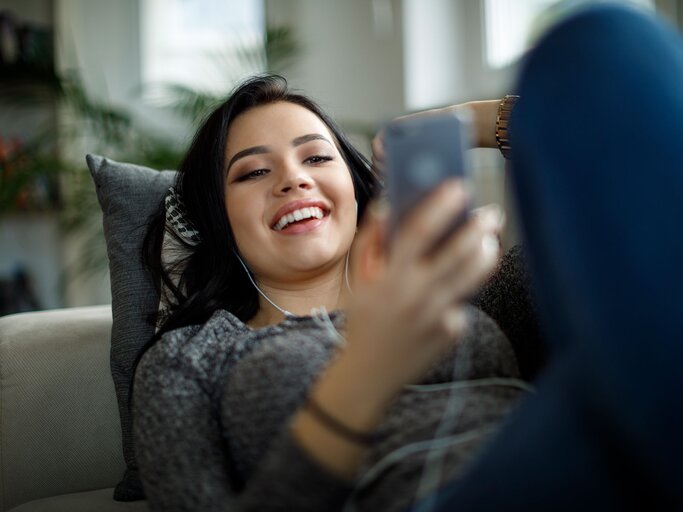 Junge Frau entspannt mit Kopfhörern und Handy auf dem Sofa | © iStock | damircudic