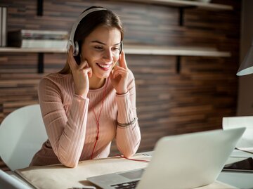 Hübsche Frau sitzt mit Kopfhörern am PC | © iStock | Georgijevic