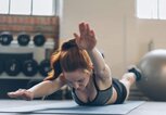 Junge Frau mit roten Haaren liegt in Sportkleidung auf dem Boden und übt die Schwimmer-Übung für die Rückenmuskulatur. | © iStock | stockfour
