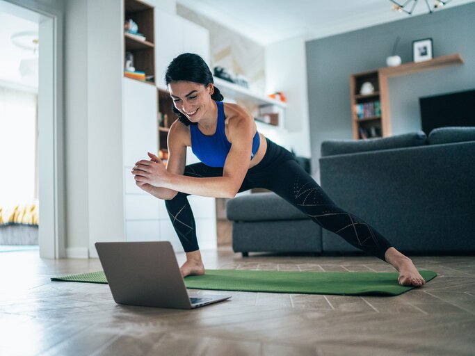 Frau trainiert mit Laptop im Wohnzimmer | © iStock | filadendron