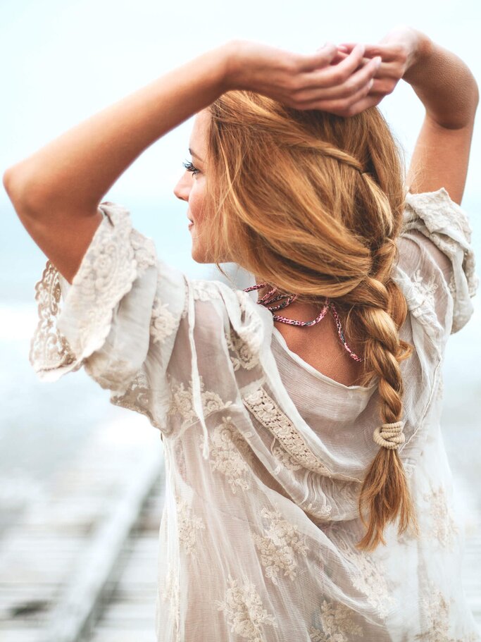 Frau steht auf einem Steg, trägt ein weißes luftiges Oberteil und hat ihre Haare zu einem tiefen Zopf geflochten. | © iStock | Jasmina007