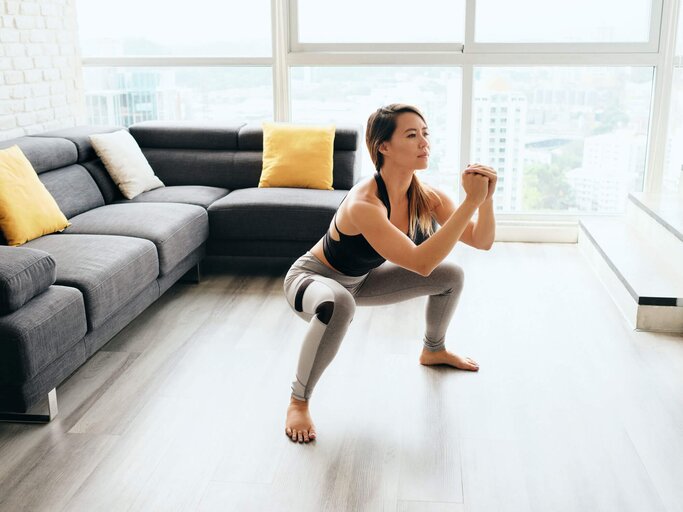 Junge Frau übt in ihrem Wohnzimmer barfuß Sumo Squats. | © iStock | diego_cervo