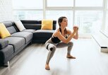 Junge Frau übt in ihrem Wohnzimmer barfuß Sumo Squats. | © iStock | diego_cervo