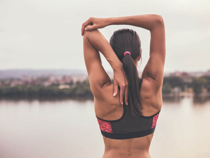 Sportliche Frau dehnt sich am See. | © iStock | LittleBee80