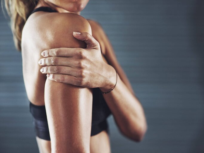 Sportliche Frau hält sich den rechten Oberarm. | © iStock | PeopleImages