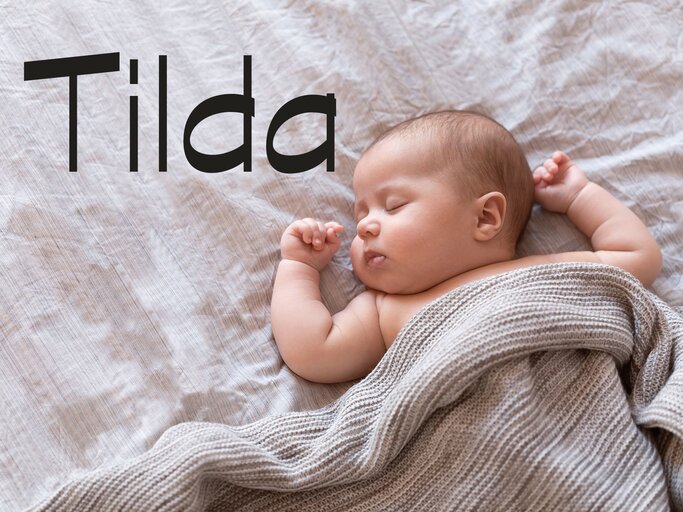 Baby liegt im Bett - dazu der Name Tilda | © iStock | Amax Photo
