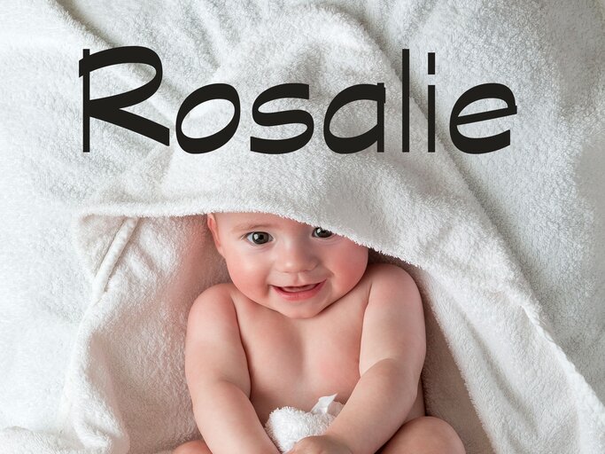 Baby liegt mit einem Handtuch eingewickelt im Bett - dazu der Babyname Rosalie | © iStock | SolStock