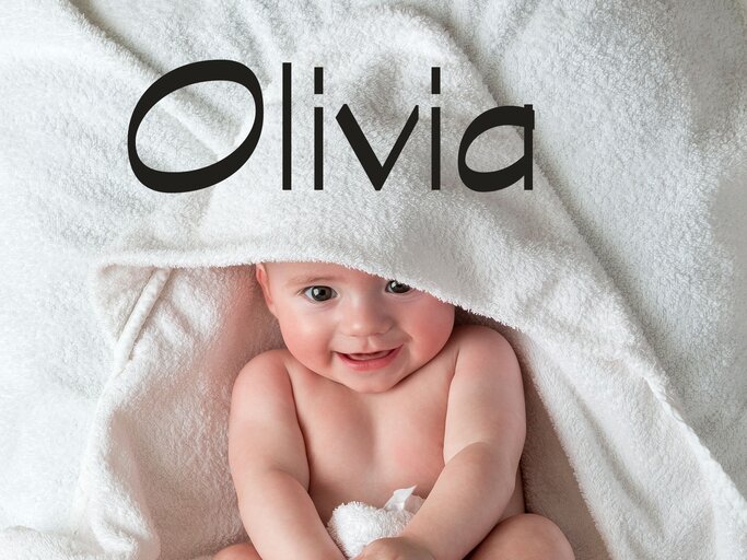 Baby liegt mit einem Handtuch eingewickelt im Bett - dazu der Babyname Olivia | © iStock | SolStock