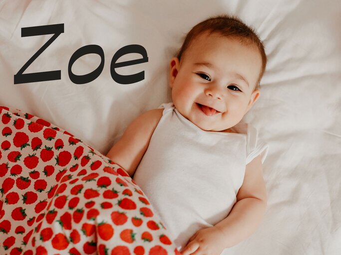 Glückliches Baby liegt im Bett - dazu der Name Zoe | © iStock | ozgurcankaya