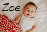 Glückliches Baby liegt im Bett - dazu der Name Zoe | © iStock | ozgurcankaya