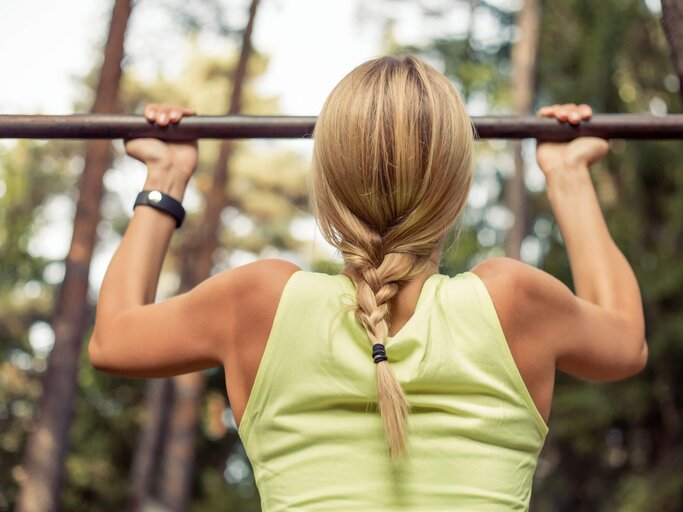 Blonde Frau mit gelben Oberteil macht Klimmzüge im Wald. | © iStock | grinvalds