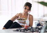 Junge Frau im Sportoutfit sitzt in der Küche und isst Salat. | © iStock | nensuria