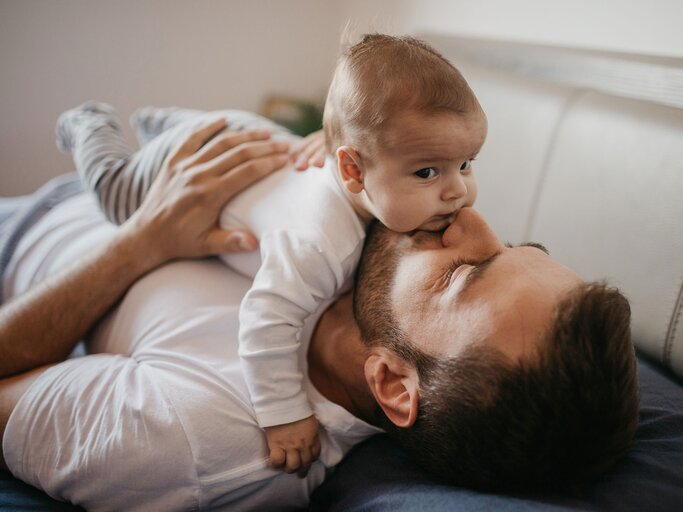 Vater liegt mit seinem Baby auf dem Bett und kuschelt | © iStock | Anchiy