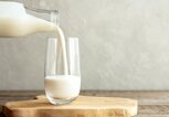 Kefir, Milch oder türkisches Ayran-Getränk werden aus einer Flasche in einen Glasbecher gegossen. Ein Glas steht auf einem Holzständer auf einem rustikalen Holztisch. | © iStock | Elena Medoks