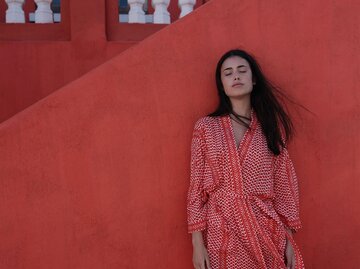 Junge Frau mit einem rot-gemusterten Kleid von lala Berlin steht für einer roten Wand. | © lala Berlin