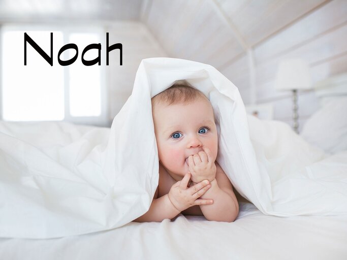 Süßes Baby mit Bettdecke auf dem Kopf und dem Namen Noah | © iStock.com | KristinaKibler