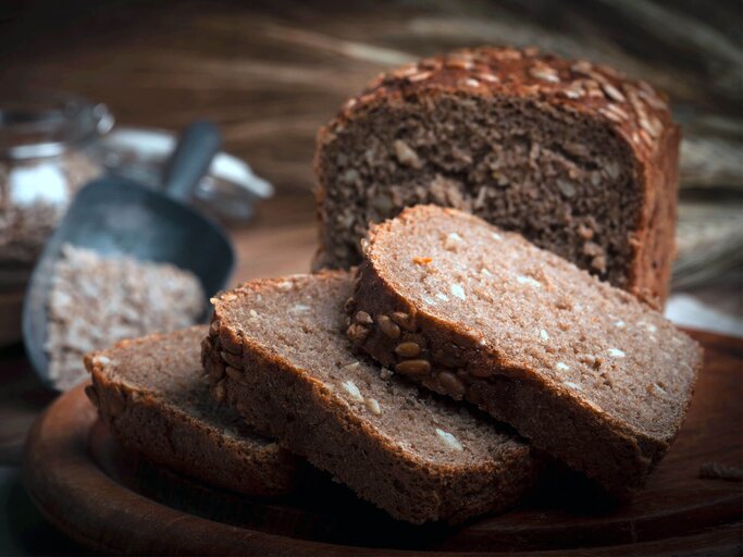 Aufgeschnittenes Vollkornbrot auf rustikalem Holzbrett. | © iStock.com / arfo