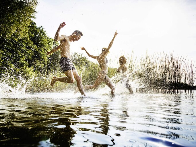 Freunde, die zusammen im Wasser im See plantschen. | © iStock.com / TommL