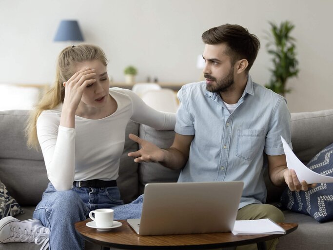 Paar diskutiert auf der Couch vor einem Laptop und Unterlagen.  | © iStock.com / fizkes