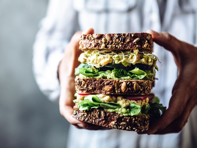 Frauenhände halten ein großes vegetarisches Sandwich mit Vollkorn | © iStock.com / alvarez