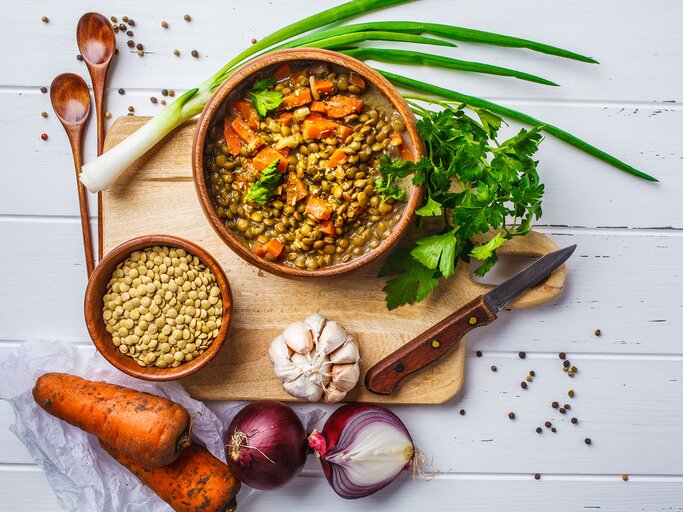 Linsensuppe in einer Holzschale und Zutaten auf einem weißen Hintergrund aus Holz | © iStock.com / vaaseenaa