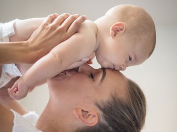 Mutter hebt ihr Kind über den Kopf und küsst es  | © iStock.com / Mladen Zivkovic