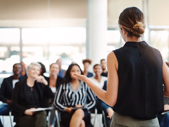 Frau hält einen Vortrag vor einer Gruppe von Menschen | © iStock.com / Cecilie_Arcurs