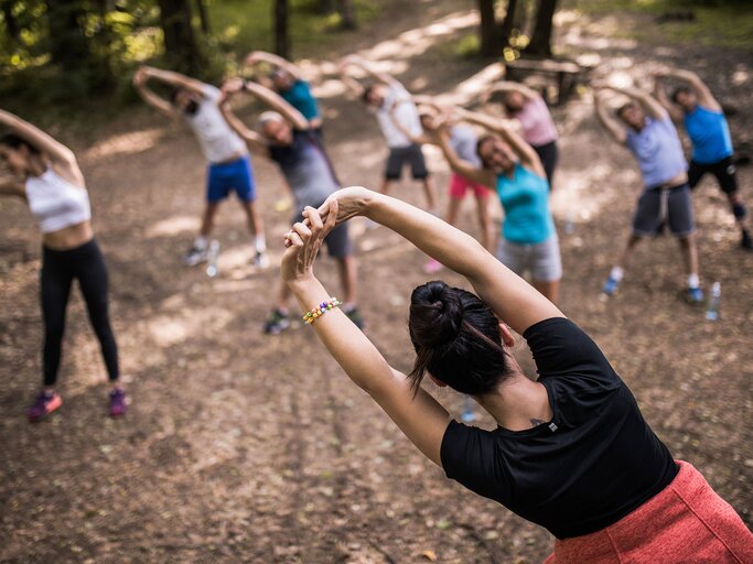 Rückansicht des Fitnesstrainers, der sich mit einer Gruppe von Menschen in der Natur aufwärmt | © iStock.com / skynesher