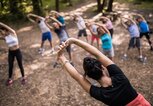 Rückansicht des Fitnesstrainers, der sich mit einer Gruppe von Menschen in der Natur aufwärmt | © iStock.com / skynesher