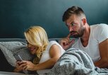 Junges Paar liegt im Bett, sie schaut auf ihr Handy | © iStock.com / blackCAT