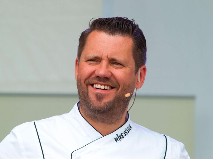Mike Süsser mit einem weißen Kochhemd.  | © imago images / Christian Schroedter