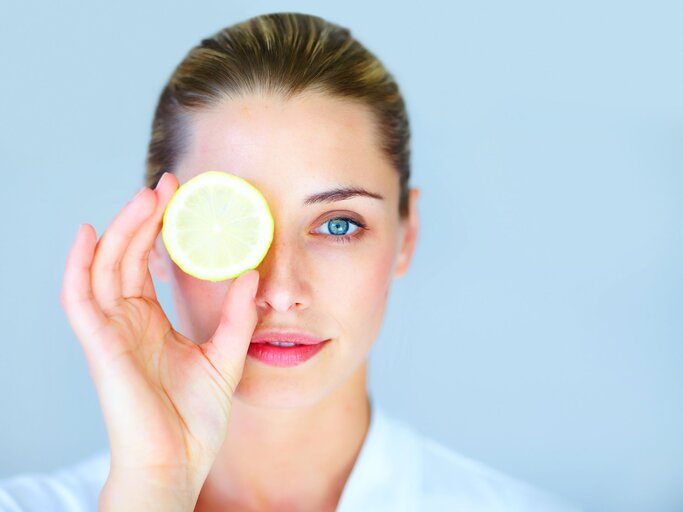 Frau hält sich eine aufgeschnittene Zitrone vor ein Auge | © iStock.com / GlobalStock
