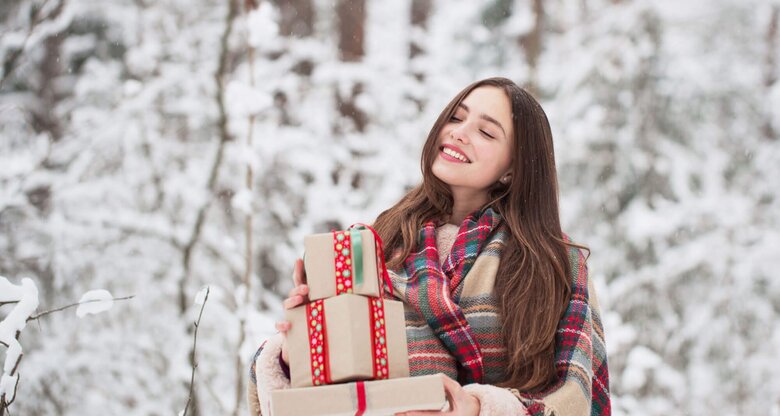 Frau steht im Schnee mit Weihnachtsgeschenken auf dem Arm.  | © iStock.com / Maya23K