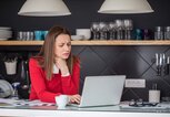 Frau mit Halsschmerzen steht in der Küche und arbeitet am Laptop. | © gettyimages.de / South_agency