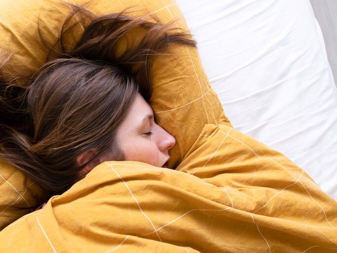 Frau liegt mit Gliederschmerzen im Bett und hat geschlossene Augen. | © gettyimages.de / Roos Koole