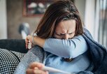 Frau sitzt warm eingepackt auf der Couch und hält ein Fieberthermometer in der Hand. | © gettyimages.de / South_agency