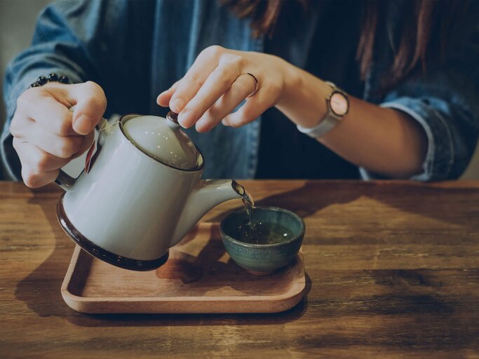 Frau schenkt sich am Tisch eine Tasse Grünen Tee ein. | © gettyimages.de / d3sign