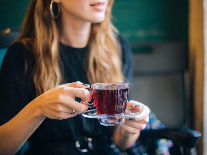 Eine Frau hält eine Tasse aus Glas in einer Hand, die roten Hagebutten-Tee enthält. | © gettyimages.de / agrobacter