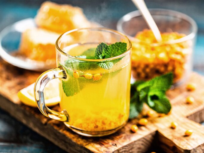 Auf einem rustikalen Holzbrett steht eine Tasse aus Glas mit frisch aufgebrühtem Sanddorn-Tee mit Minze. | © gettyimages.de / ivandzyuba