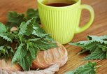 Eine gelbe Tasse mit frischem Brennnesseltee steht auf einem Holztisch. | © gettyimages.de / Vaivirga