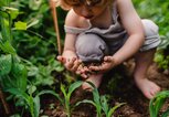 Ein Kind sitzt im Kräuterbeet und hat die Hände voller Erde. | © gettyimages.de / Halfpoint Images