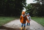 Zwei Kinder spielen an der frischen Luft, ein Kind springt mit Gummistiefeln in eine Pfütze. | © gettyimages.de / Cavan Images