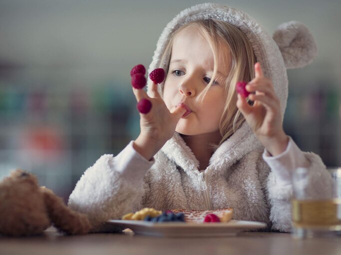 Ein Mädchen sitzt am Tisch und isst Waffeln mit frischen Beeren. | © gettyimages.de / Elva Etienne