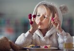 Ein Mädchen sitzt am Tisch und isst Waffeln mit frischen Beeren. | © gettyimages.de / Elva Etienne