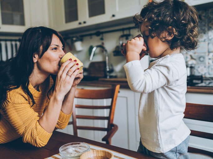 Eine Mutter und ihr Sohn trinken in der Küche aus Tassen. | © gettyimages.de / filadendron