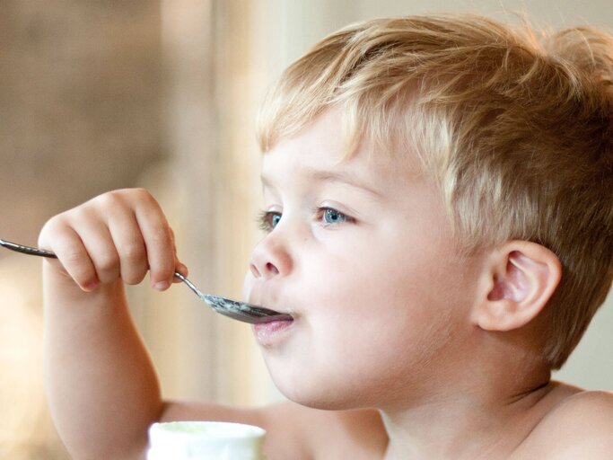 Ein blonder Junge ist Joghurt mit einem Löffel. | © gettyimages.de / Becki Bennett